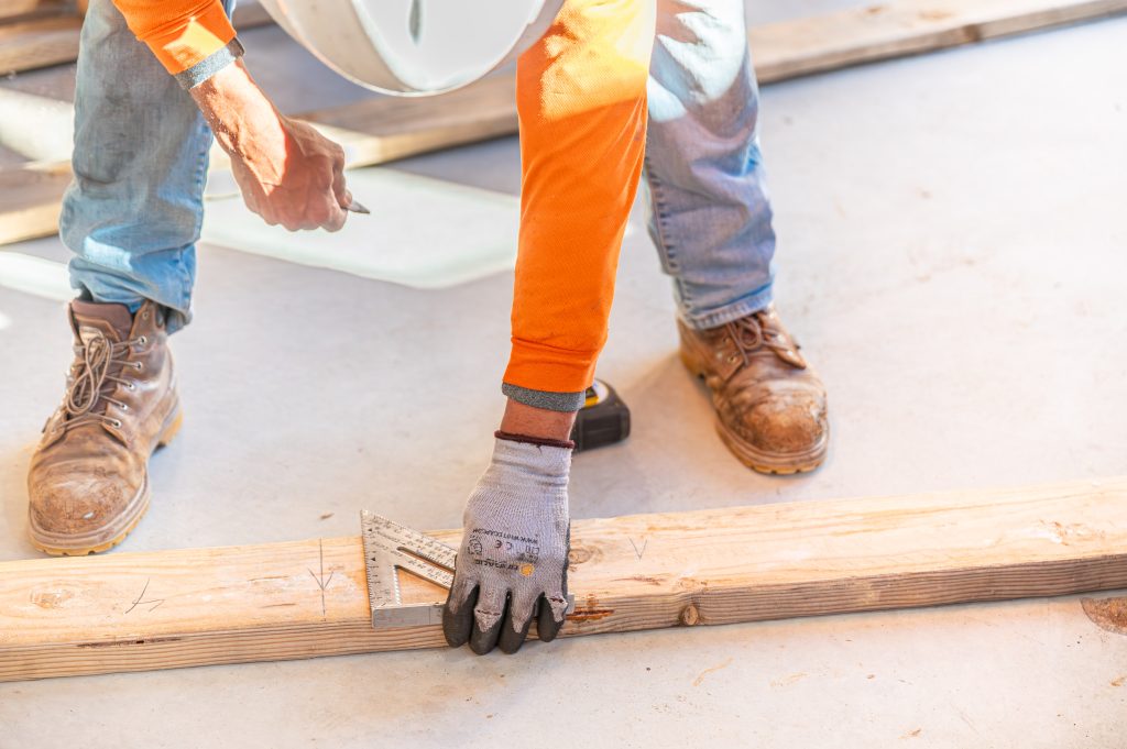 Worker hammering nails into wooden beams to form the structure of a building