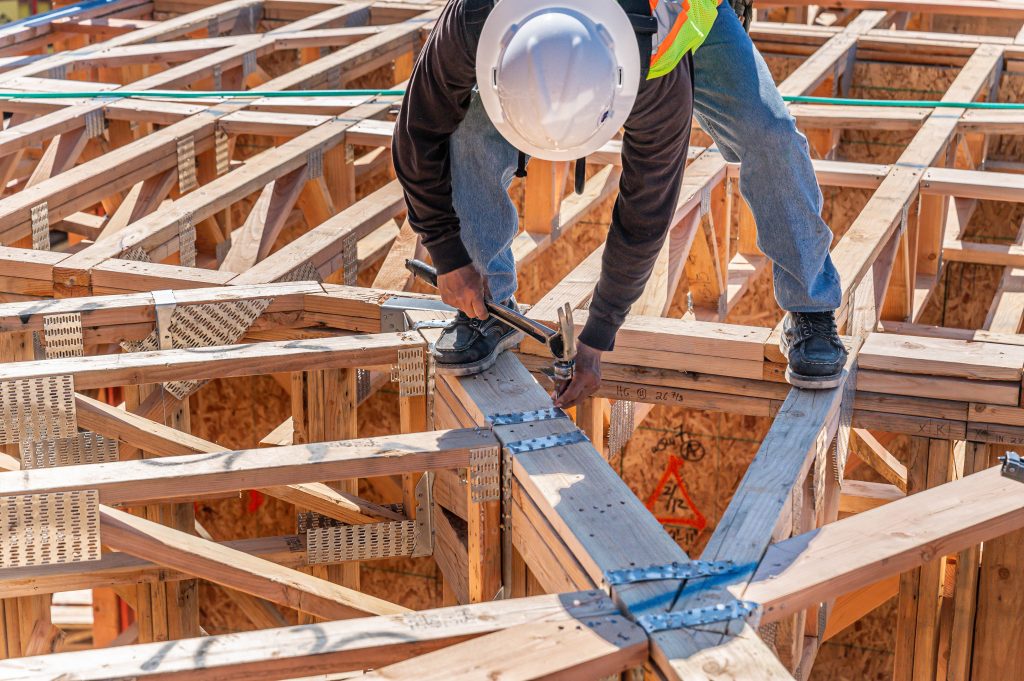 Person in a hard hat inspecting the wooden frame for a new house.