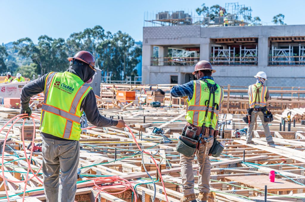 Builder using a power drill to fasten wooden frame components securely.