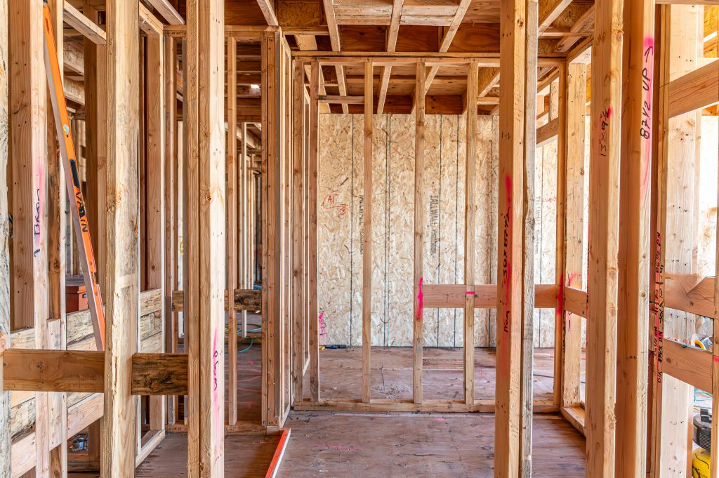 Construction worker hammering nails into wooden planks for wall framing.