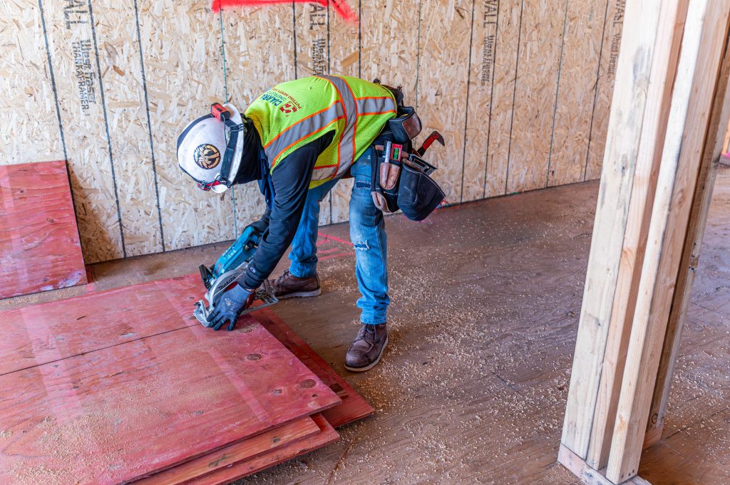 Person aligning wooden rafters and securing them with metal brackets.
