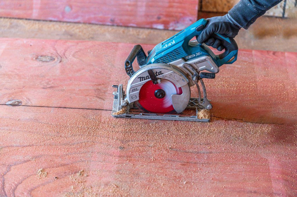 Man in safety gear using a hand saw to cut wooden planks for framing.