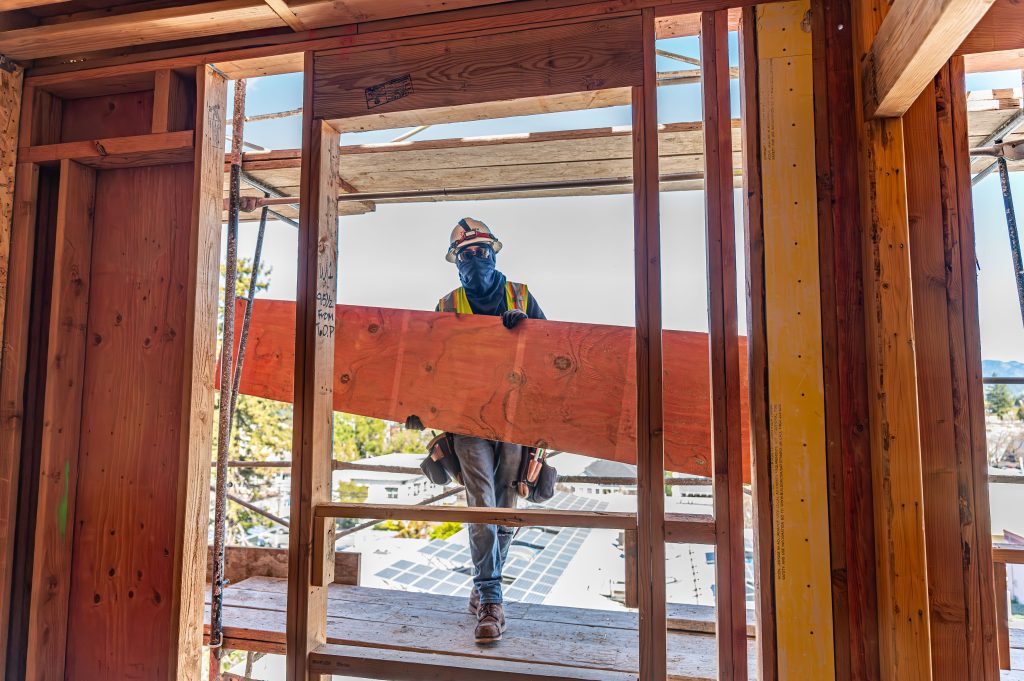 Builder installing wooden headers above window openings in a house frame