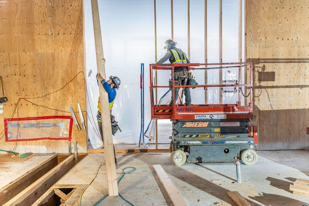 Man drilling holes into wooden beams for frame assembly