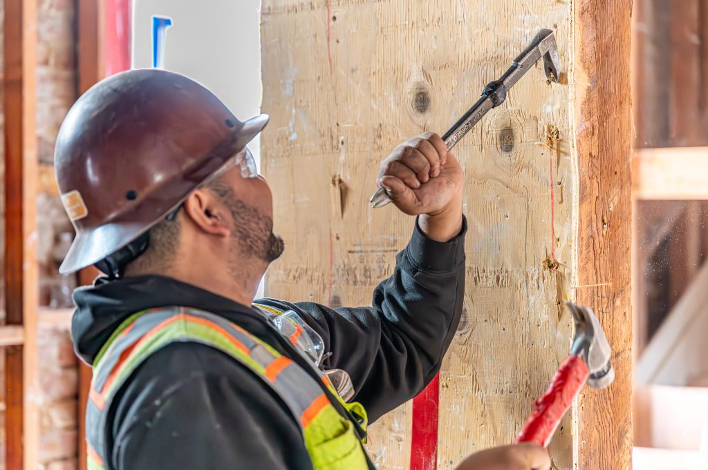 Worker in a hard hat positioning and aligning wooden framework for walls
