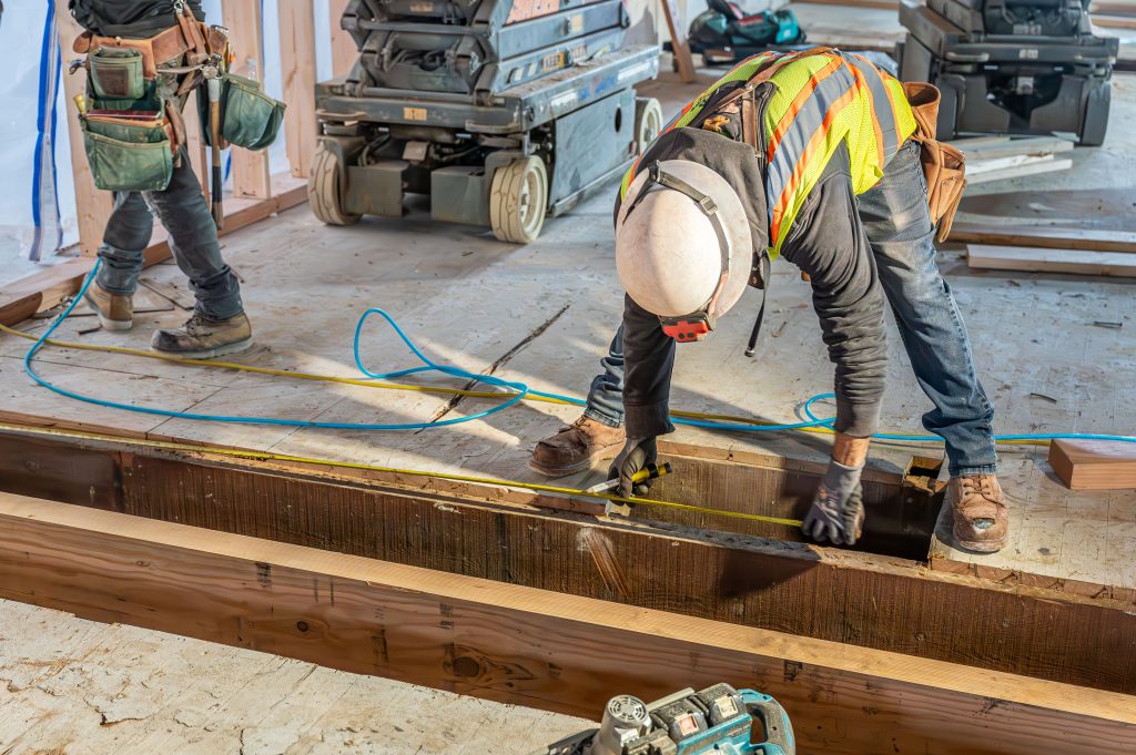 Man using a hammer to secure wooden boards into the frame of a house.