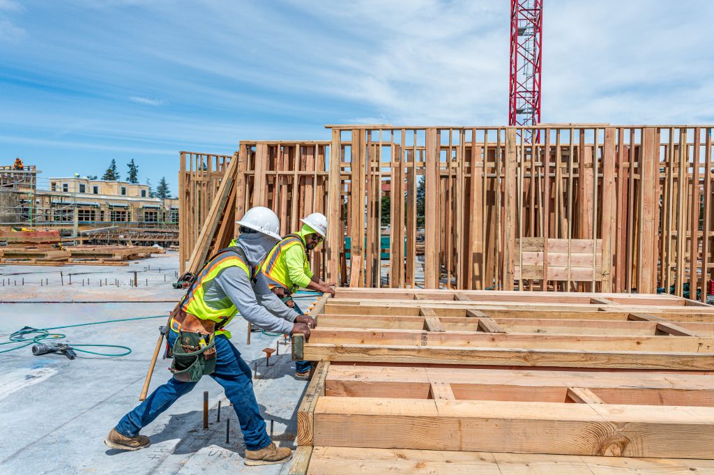 Construction worker securing wooden trusses to support the roof of a house.