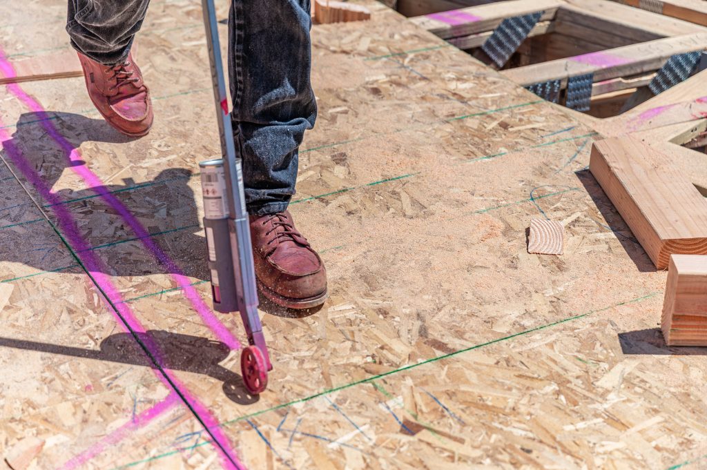 A man precisely painting a straight line on a wooden board during a construction project.