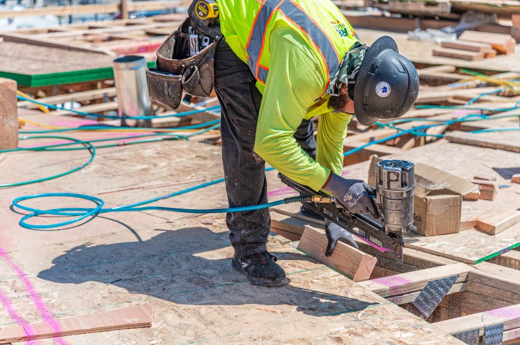 A man carefully painting a straight line on a wooden surface at a construction site.