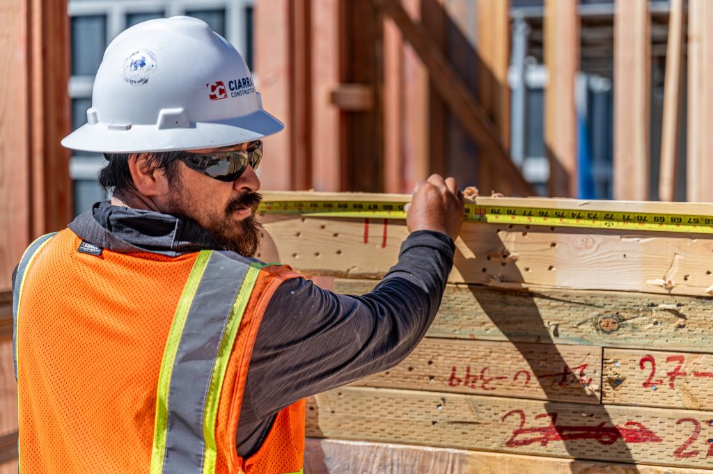 A construction worker using a tape measure to measure a wooden board