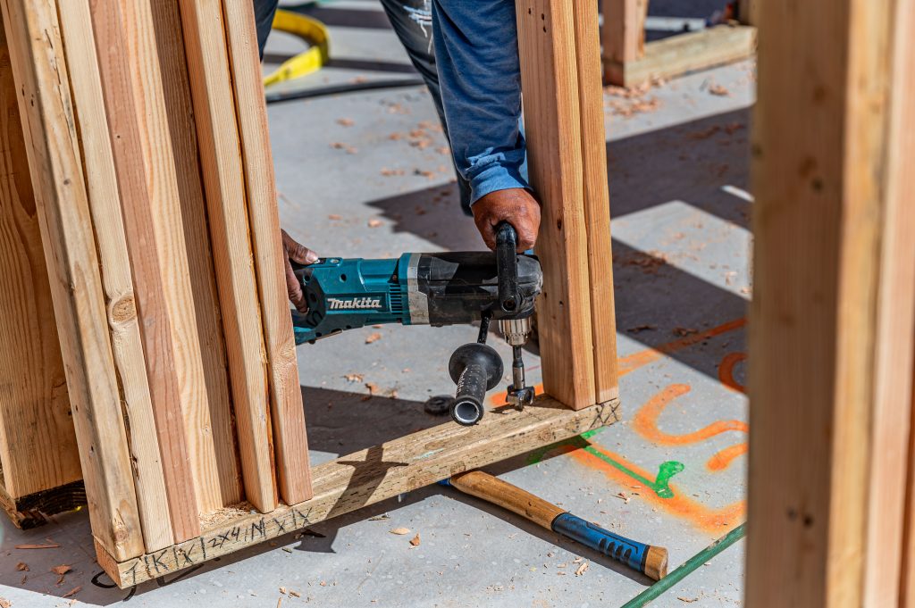 A construction worker drilling holes into wooden beams using a machine driller