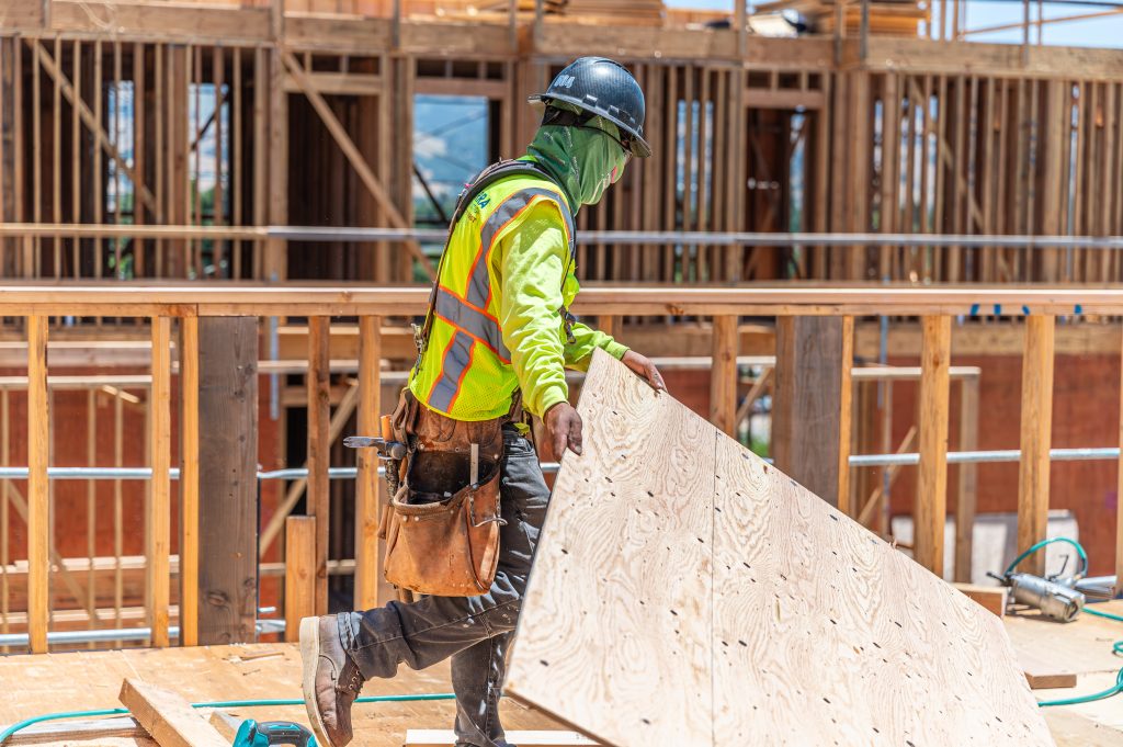 Worker in safety gear working on the wooden framework of a building.