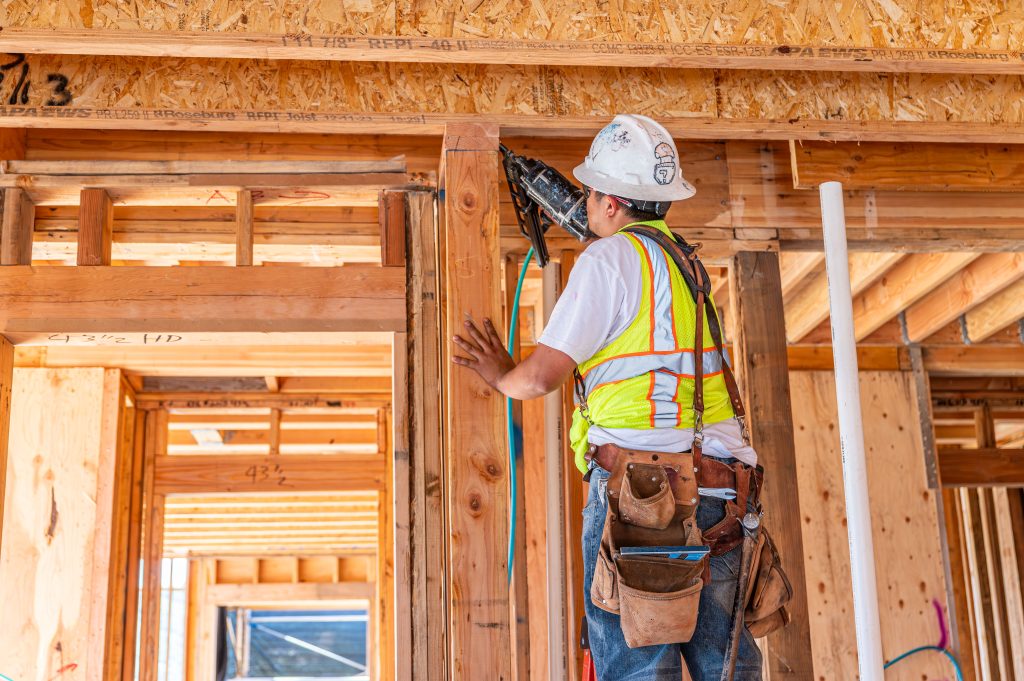 Man in a hard hat installing wooden beams on a construction site.
